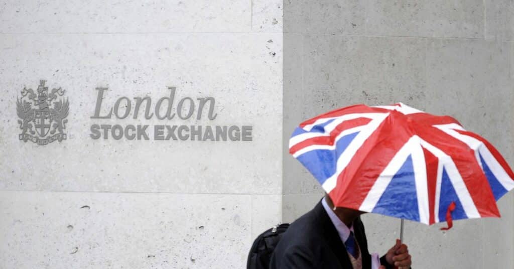 A worker shelters from the rain as he passes the London Stock Exchange in London