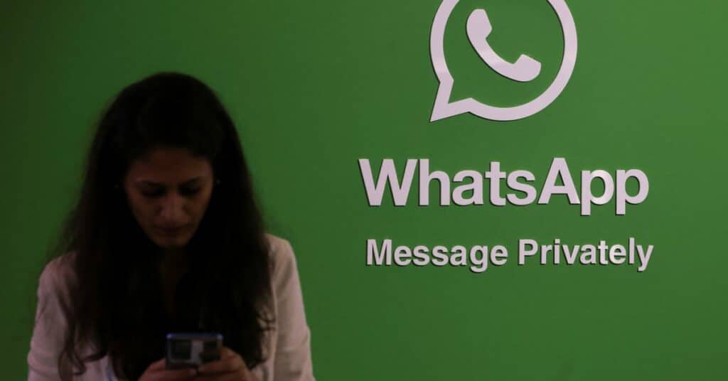 A woman uses her phone next to a logo of the WhatsApp application during Global Fintech Fest in Mumbai