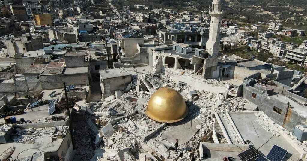 People stand near a damaged mosque in rebel-held al-Maland village